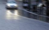 Blurred image of a car driving in rain along a tarred urban road at night with headlights shining and copy space