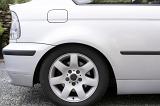 Close up of rear car wheel on white automobile parked in driveway by bushes