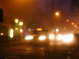 Blurry street scene at night with bright streetlights and headlights from various vehicles