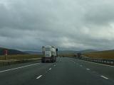Back view of lonely truck riding on highway in fields on cloudy gloomy day.