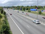 Cars travelling on a three lane motorway in countryside with a garage or service station on the one side