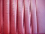 Red leather car seat background texture wit vertical ridges and stitching in a full frame view