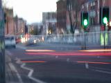 Blurred background of a city street at dusk with light trails of traffic and a green traffic light at an intersection