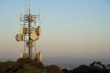 Cellular or mobile phone communications mast or tower with dish antennae with transmitters and receivers on a hilltop at sunset