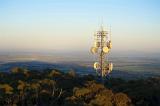 Mobile phone communications mast on a forested hilltop with dish antennae in an open landscape at sunset