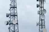 Two mobile phone masts with dish antennae for transmitting and receiving radio signals in a communications concept close up against a grey cloudy sky
