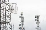 Three mobile telecommunications towers in mist or cloud with dish antennae to receive and transmit radio signals