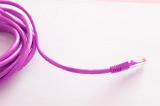 Bright vivid pink computer network cable and plug coiled on a white background with copy space in a communications concept