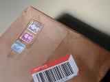 Cancelled British postage stamps on a brown paper parcel with bar code in a partial close up view from the top in a communication concept