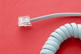 Plug connector and coiled white spiral cord or cable for a telephone on a red background with copy space