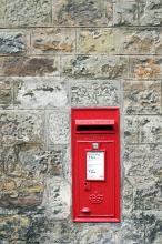 Red Royal mail letterbox in an old stone wall with the times of collection on the front in a communication concept