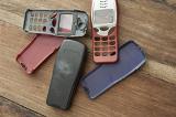 Collection of old retro cellphone or mobile phone covers or cases in assorted colors for button keypads, some damaged, lying on a wooden desk - not property released
