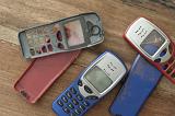 Assorted red, blue and black cases or covers for a retro button style mobile phone or cellphone lying loose on a wooden table, some with cracks and damage - not property released