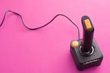 Retro black and orange joystick over pink background with copy space. Cord reaching around top side.