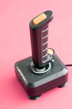 Joystick with cable standing against pink background