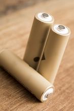Three natural coloured AA rechargeable cell batteries isolated on a brown timber background.