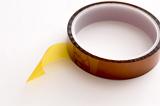 Roll of yellowish Kapton tape with end detached close-up on white table surface
