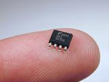 Small black integrated circuit chip on tip of a finger - macro detail view on grey background