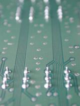 A close up of the underside of an electronic circuit board showing deductive tracks, wiring and solder joints.