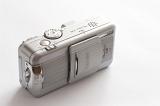 Silver compact camera with retracting lens behind a sliding cover viewed high angle on white with copy space