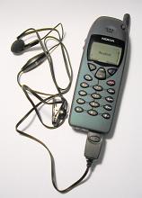 Old Nokia push button mobile phone with earpiece or earplug attached by a cord for audio lying on a white background - editorial use only