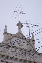 Antenna on the roof of an historic stone building viewed from below with power cables in the foreground in a communications concept