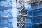 Commercial high-rise building maintenance and repair concept with scaffolding and protective plastic sheeting obscuring the sides of a building