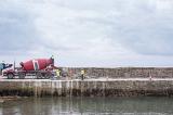Cement mixer truck with workmen on a concrete wharf or quay in a concept of marine construction under a cloudy sky