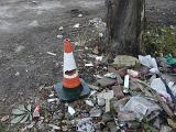 Damaged traffic cone and pile of rubbish alongside a wooden pole in a concept of pollutants and environmental pollution