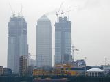 Industrial construction on three tall skyscrapers in an urban environment with heavy duty machinery and tall cranes against a misty skyline