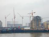 Constructing site with a lot of office and residential buildings under construction and many cranes on the bank, viewed from the water against smoky grey sky