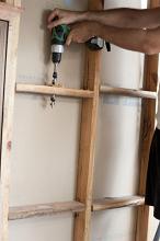 Man drilling wire hole in stud wall with a battery drill, holding it with both hands
