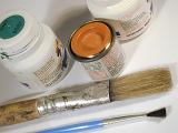 Small cans of paint and clean brushes of different sizes viewed in close-up on white background