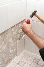 Man removing old wall tiles using a hammer and screwdriver to prise them from the wall after first removing the grout
