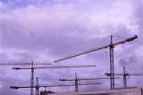 Many construction cranes against purple stormy clouds, viewed from low angle