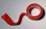 Red insulating tape with wavy unrolled end viewed in close-up from above on grey background