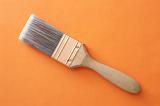 Clean new interior decorating paint brush with fine bristles and a wooden handle lying diagonally on an orange background with copy space