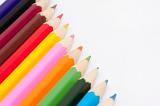 Row of coloured pencil crayons in the colours of the rainbow in a diagonal line with copyspace on a white background