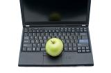 Distance learning concept depicting an open laptop, with a green apple resting on the keyboard, on a white background