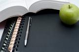 Education and learning background with a fresh healthy green apple alongside an open book with a pen and spiral binders