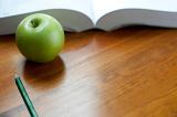 Fresh green apple with an open textbook and pencil on a wooden desktop in an educational concept with copyspace