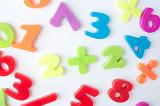 Preschool maths education concept with colourful plastic numbers and symbols scattered on a white surface