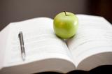 A fresh juicy green apple stands on an open textbook with a pen conceptual of education and learning