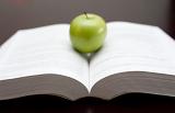 Fresh green apple balanced on the open pages of a textbook or novel in an education and learning or relaxation and reading concept