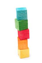 Wooden toy building blocks, in bright colours over white background, stacked in a tower