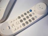 White handset of a land line telephone off the hook lying on a white surface with the keypad uppermost