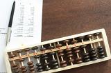 Pen and printed expense report beside wooden abacus over brown table with copy space