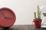 Business deadline concept with a modern minimalist red clock on a desk alongside a potted plant in a small pail or bucket, with copy space