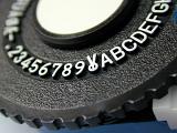 Macro view of the numbers and letters on a Dymo tape wheel for printing embossed labels with the snip tool in the center