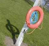 Red lifesaver or life ring hanging on a pole with attached blue rope for use as a flotation device in the rescue of a drowning person